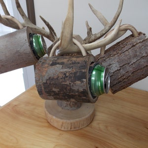 May include: A wooden beer holder made from tree branches and antlers. The holder has four slots for cans and a wooden base.