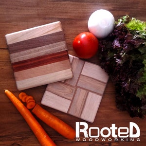 May include: Two small wooden cutting boards, one with a striped pattern and the other with a checkered pattern. The boards are on a wooden surface with a red tomato, a white onion, and a bunch of red lettuce.