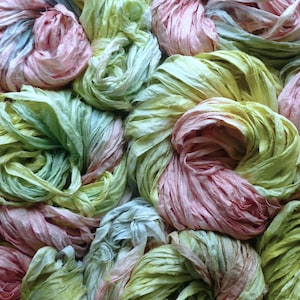 May include: A close-up of a pile of colourful, textured fabric. The fabric is arranged in loose, circular bundles. The colours include shades of pink, green, yellow, and blue, creating a soft, pastel palette. The fabric appears to be silk or a similar material.