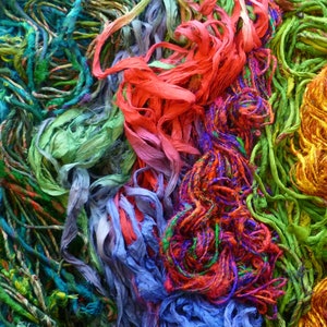 May include: A close-up of a colorful assortment of yarn and string in shades of green, blue, red, orange, and yellow. The yarn is arranged in a random pattern, creating a visually appealing and textured background.