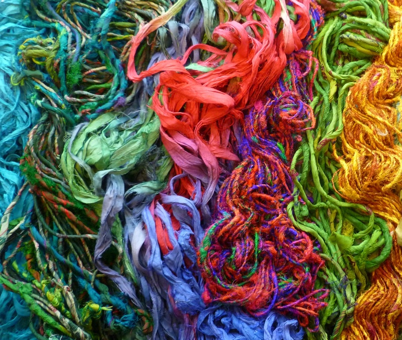 May include: A close-up of a colorful assortment of yarn and string in shades of green, blue, red, orange, and yellow. The yarn is arranged in a random pattern, creating a visually appealing and textured background.