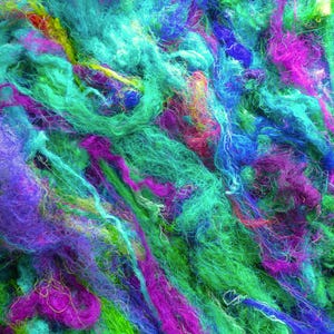 Könnte beinhalten: Ein dichtes, verheddertes Knäuel aus losen Textilfasern in leuchtenden Türkis-, Elektroblau-, Magenta-, Limettengrün- und Violetttönen. Die Fasern sind fein, fusselig und miteinander verflochten, was eine strukturierte, bunte Garnoberfläche ergibt.