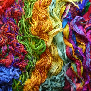May include: A colorful assortment of silk ribbon scraps in shades of red, orange, yellow, green, blue, purple, and pink. The ribbons are tangled and overlapping, creating a vibrant and textured background.