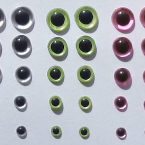 Puede incluir: Surtido de ojos saltones de pl&aacute;stico en varios tama&ntilde;os y colores, incluyendo transparente, verde y rosa. Los ojos est&aacute;n dispuestos en filas por tama&ntilde;o y color.