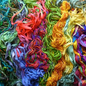 May include: A collection of colorful silk ribbons and threads in various shades of green, blue, red, yellow, and purple. The ribbons are tangled and intertwined, creating a vibrant and textured display.