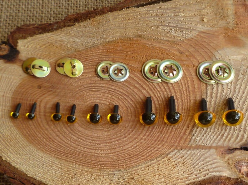 May include: Assortment of plastic safety eyes in various sizes, with black pupils and amber colored irises. The eyes are attached to black plastic posts. Also included are metal fasteners for attaching the eyes to fabric.