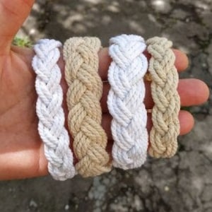 May include: Four braided rope bracelets in two colors: white and beige. The bracelets are made of thick, woven rope and are a simple, stylish accessory.