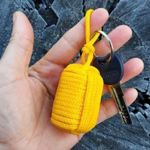 May include: A yellow paracord keychain with a black key attached. The keychain is made of braided paracord and has a loop for attaching to a key ring.