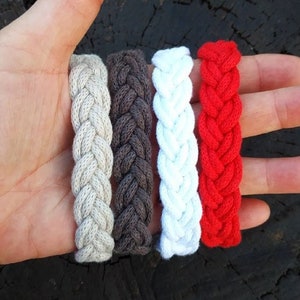 Peut inclure: Quatre bracelets en corde tressée de différentes couleurs : beige, marron, blanc et rouge.