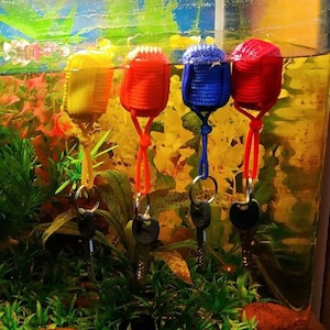 Puede incluir: Cuatro llaveros coloridos colgando en un tanque de peces. Los llaveros están hechos de hilo y tienen una llave unida a la parte inferior. Los llaveros son rojo, amarillo, azul y verde.