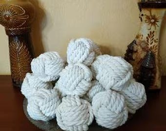 May include: A collection of white rope balls, arranged in a circular pattern on a wooden surface. The balls are made of thick, white rope and are tied into a knot at the centre.