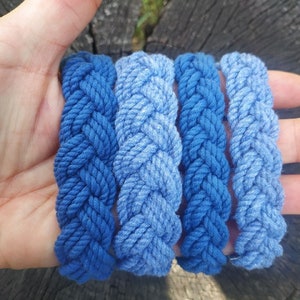 May include: Four blue braided rope bracelets, stacked on top of each other, with a gradient of blue shades.