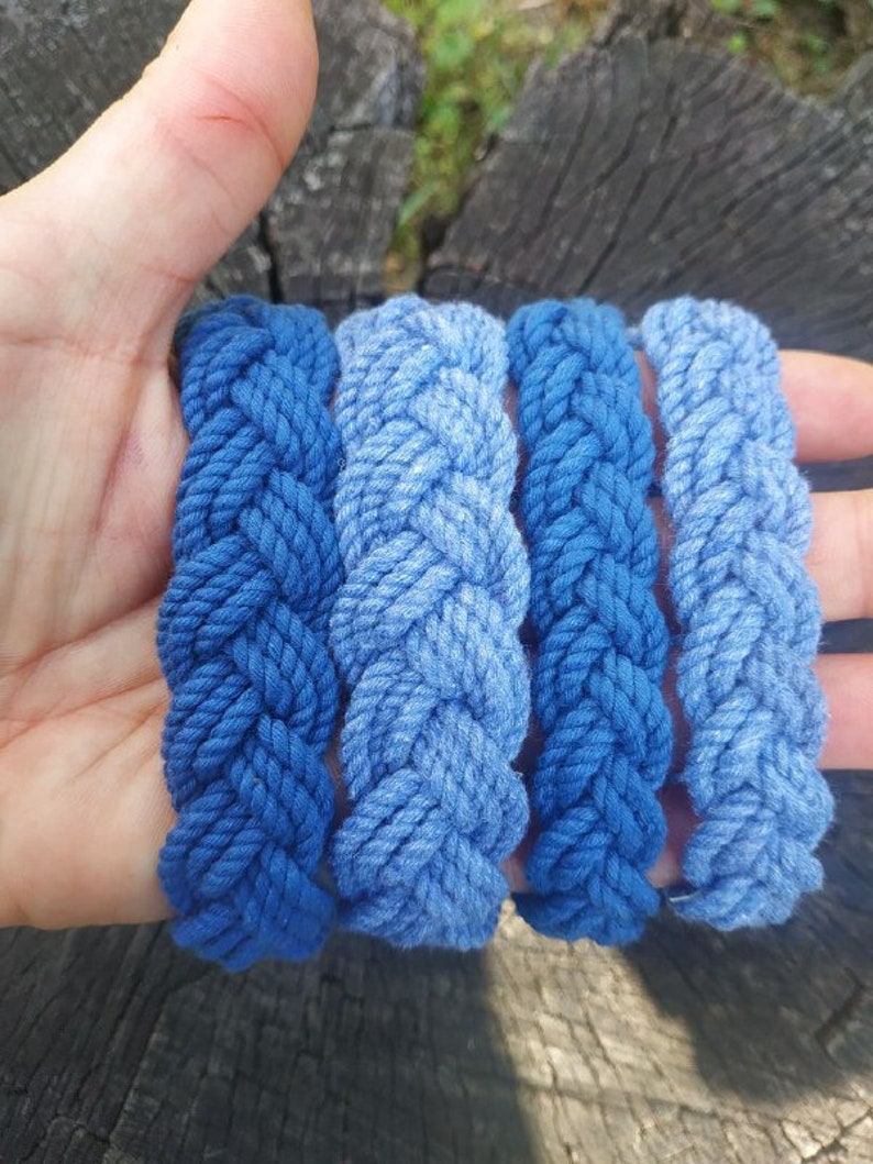 May include: Four blue braided rope bracelets, stacked on top of each other, with a gradient of blue shades.