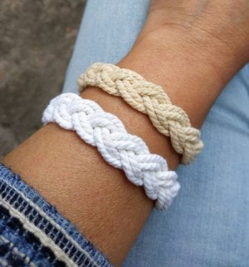 May include: Two braided rope bracelets, one white and one beige, worn on a wrist.