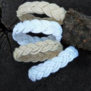 May include: Four braided rope bracelets in white and beige colors. The bracelets are stacked on top of each other.