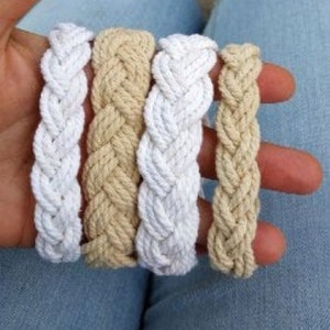 May include: Four braided rope bracelets in white and beige. The bracelets are made of thick rope and have a simple, classic design.