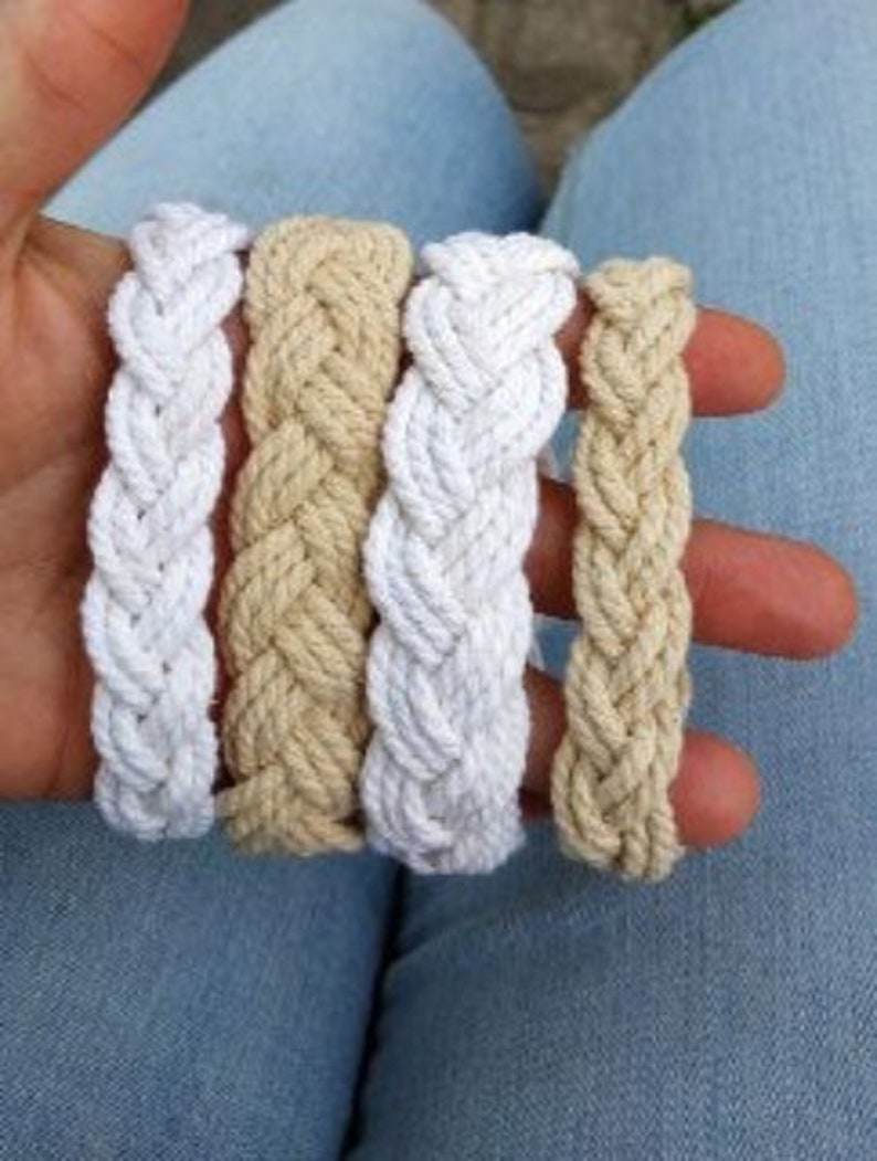 May include: Four braided rope bracelets in white and beige. The bracelets are made of thick rope and have a simple, classic design.