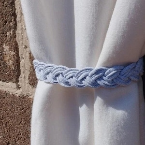 May include: A light blue braided rope curtain tieback. The tieback is tied around a white curtain.