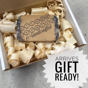 May include: A cardboard box filled with wood shavings, containing a small, rectangular package. The package has a typewriter-style design with the words "SILVER EXPRESS Handcrafted". The image also includes the text "ARRIVES GIFT READY!"