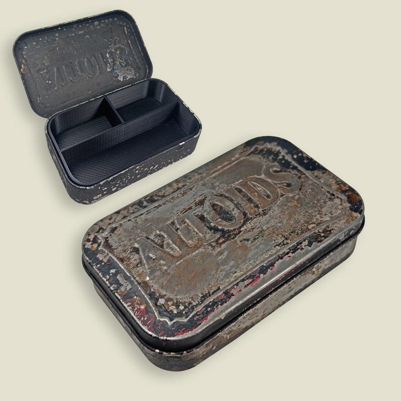 May include: Two vintage Altoids tins, one open and one closed, with a distressed, rusty appearance. The open tin reveals a black interior with dividers. The tins have a rectangular shape and are likely made of metal.