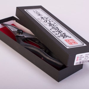 May include: A black box with a pair of silver pruning shears inside. The box has Japanese text on it that reads "おの剪定鋏" and "高級品". The box also has a barcode and the text "AN-200-2".