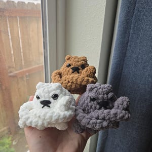 May include: Three handmade crochet bears in white, brown, and gray. Each bear has a grumpy expression with black eyes and a stitched mouth. The bears are made of soft, chunky yarn.