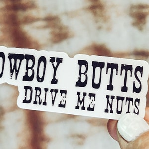 May include: White sticker with black text that reads "Cowboy Butts Drive Me Nuts".