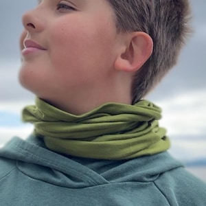 May include: A young person wearing a green hooded sweatshirt with a green neck gaiter. The person is looking up and to the right.