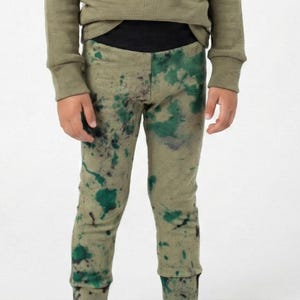May include: Olive green long-sleeved top and leggings set. The leggings feature a unique pattern of green and purple splatters against a light olive background. The set is made of a soft, comfortable material.