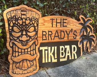 May include: A wooden tiki bar sign with a carved tiki head, palm trees, and the text "The Brady's Tiki Bar".