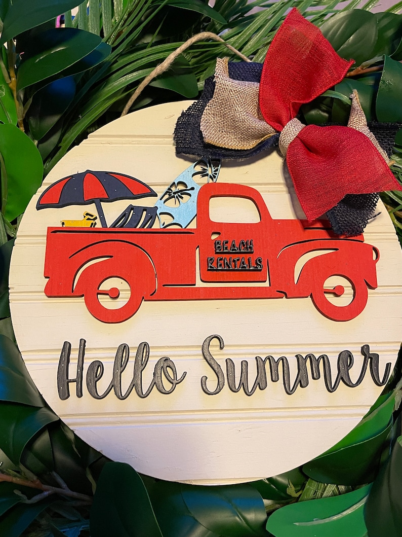 Pu&ograve; includere: Un cartello rotondo di legno con un camioncino rosso che trasporta tavole da surf e un ombrello. Il camioncino ha la scritta "Beach Rentals" sul lato. Il cartello ha anche la scritta "Hello Summer" in lettere nere.