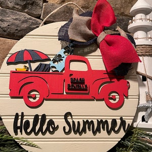 Pu&ograve; includere: Un cartello rotondo in legno bianco con un camioncino rosso che trasporta tavole da surf e un ombrello. Il camioncino ha la scritta "Beach Rentals" sul lato. Il cartello ha anche la scritta "Hello Summer" in lettere nere.