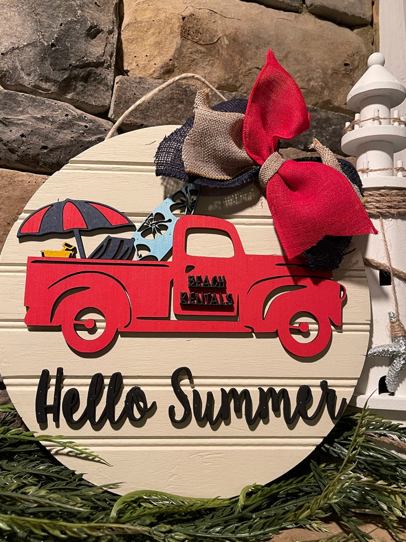Pu&ograve; includere: Un cartello rotondo in legno bianco con un camioncino rosso che trasporta tavole da surf e un ombrello. Il camioncino ha la scritta "Beach Rentals" sul lato. Il cartello ha anche la scritta "Hello Summer" in lettere nere.