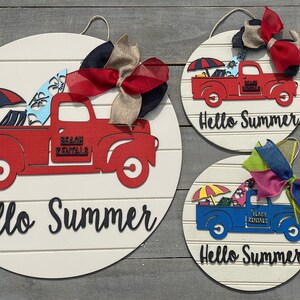 Pu&ograve; includere: Tre cartelli rotondi in legno con sfondo bianco e lettere nere che dicono "Hello Summer". Ogni cartello presenta un camion rosso, blu o bianco con una tavola da surf, un ombrello da spiaggia e le parole "Beach Rentals" sul lato. I camion sono decorati con fiocchi colorati.