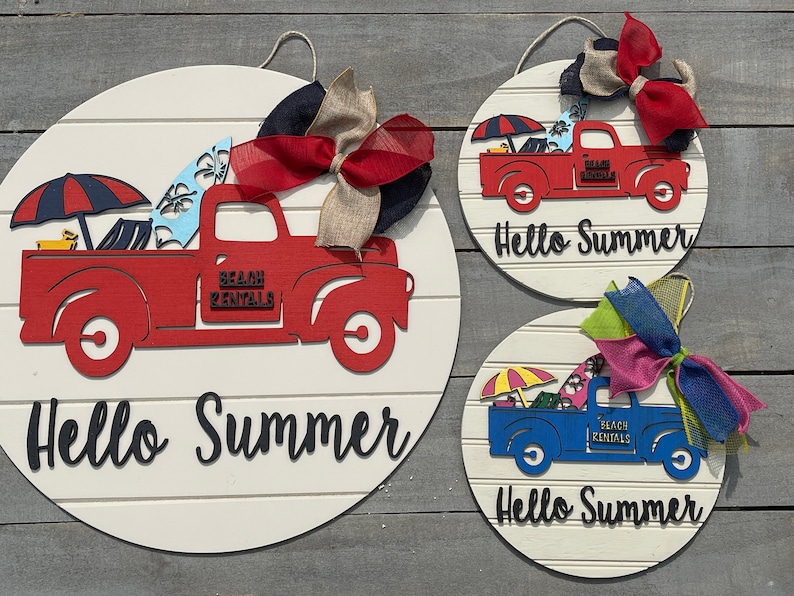 Pu&ograve; includere: Tre cartelli rotondi in legno con sfondo bianco e lettere nere che dicono "Hello Summer". Ogni cartello presenta un camion rosso, blu o bianco con una tavola da surf, un ombrello da spiaggia e le parole "Beach Rentals" sul lato. I camion sono decorati con fiocchi colorati.