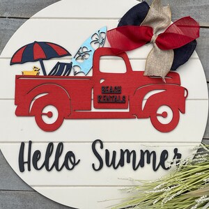 Pu&ograve; includere: Un camioncino rosso vintage con una tavola da surf, un ombrello da spiaggia e sedie da spiaggia nel cassone. Il camioncino ha la scritta "Beach Rentals" sul lato. Il camioncino &egrave; su uno sfondo di legno bianco con le parole "Hello Summer" scritte sotto.