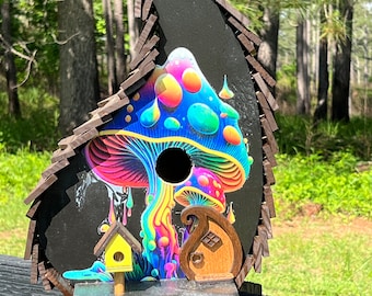 May include: A wooden birdhouse shaped like a mushroom with a psychedelic rainbow design. The birdhouse has a small yellow house and a brown house on the front.
