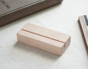 May include: A light brown wooden display stand with a slot in the centre for holding cards or photos.