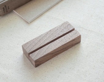 May include: A wooden display stand with a slot for holding cards or photos. The stand is made of dark brown wood and has a natural finish.