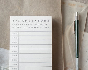 May include: A white notepad with a monthly calendar and hourly schedule from 6:00 AM to 2:00 PM. The calendar shows the months of the year, and the schedule has lines for each hour.