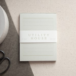 May include: A white notepad with a grid pattern and the text "UTILITY HOUSE EST 2018 RULE-DOT" printed on the front.