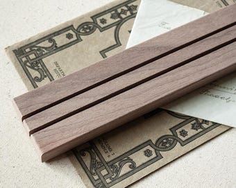 May include: A light brown wooden desk organiser with two parallel grooves. The organiser sits on vintage paper with decorative borders and a handwritten note. The organiser is approximately 25 cm long.