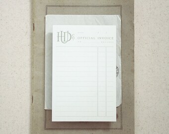 May include: A white notepad with a grey logo and the text "H.D. CO. OFFICIAL INVOICE" at the top. The notepad is sitting on a brown surface.