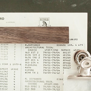 May include: A close-up of a student record card with a silver binder clip. The card lists courses, dates, and grades for an architectural technology programme. The text on the card includes "M. Difranco Architectural Tech. Course Bld Est 2 79/01-79/04 AR237".