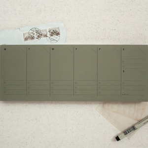 May include: A green weekly planner with days of the week labeled M, T, W, T, F, S. The planner has lines for writing tasks or appointments.