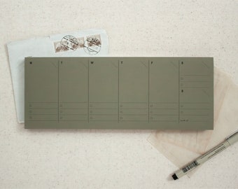 May include: A green weekly planner with days of the week labelled M, T, W, T, F, S. The planner has lines for writing tasks or appointments.