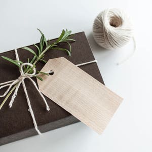 May include: A brown gift box tied with twine and decorated with a sprig of rosemary. A blank brown gift tag is attached to the box.