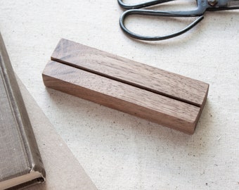 May include: A wooden display stand with a slot in the centre. The stand is made of dark brown wood and has a smooth, polished finish.
