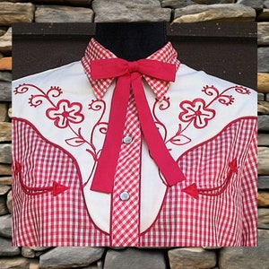 May include: A long-sleeved shirt featuring a red and white gingham pattern, a white yoke with red floral embroidery, a pointed collar, a red ribbon bow tie at the neck, and silver-toned snap buttons down the front placket.