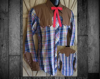 May include: A long-sleeve button-up shirt featuring a brown yoke and brown cuffs, paired with a plaid pattern in blue, yellow, and white. The shirt includes a bright red ribbon tie at the collar and metallic snap buttons on the cuffs and front.